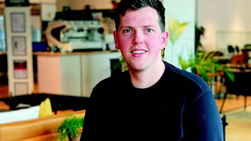 Ollie Coburn is a wearing a navy jumper and is smiling at the camera.